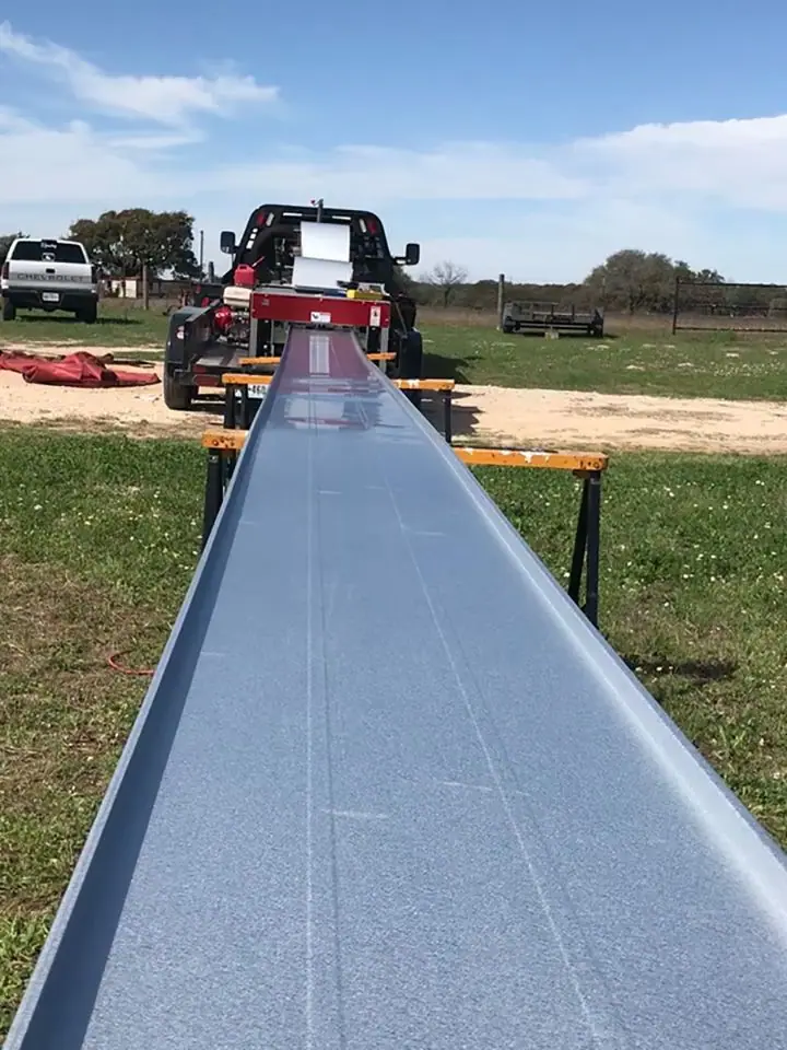 A long metal roof panel running out of the roll former on a job site